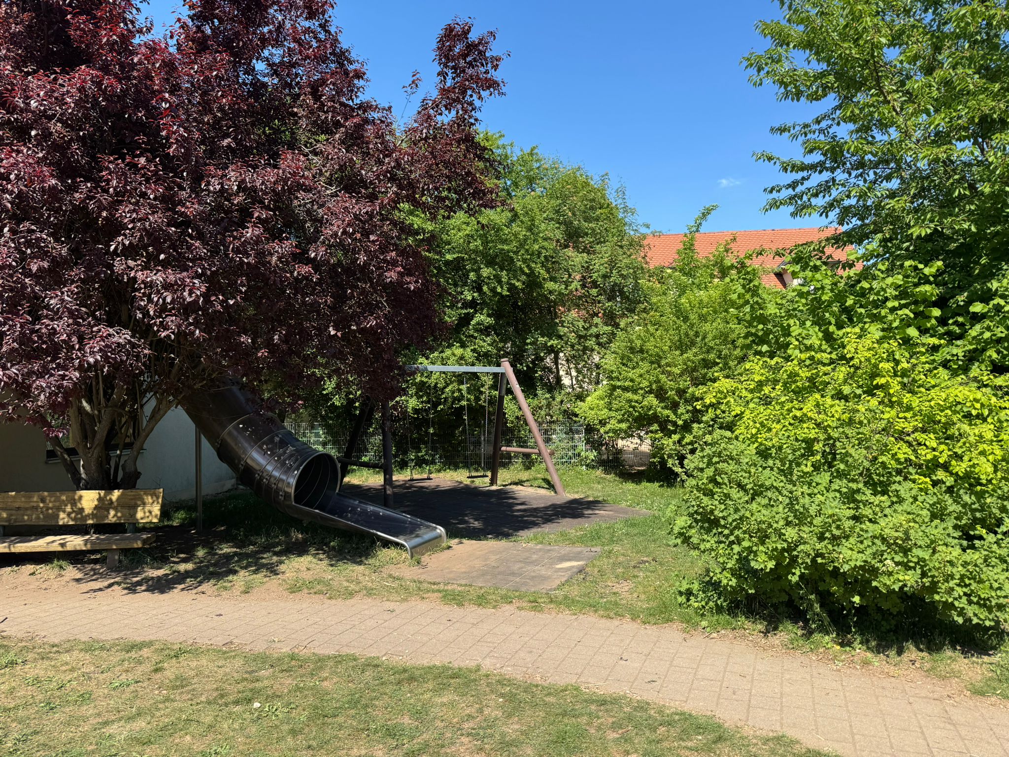 Im Garten steht an einem sonnigen Tag eine Holzschaukel.
